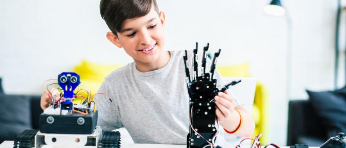 Młody człowiek stojący przy biurku, na którym stoi ręka robota.