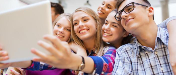 Grupa młodych, uśmiechniętych osób obserwujących coś na laptopie