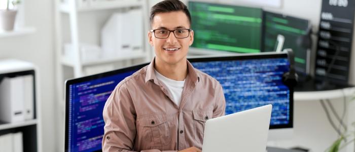 Młody człowiek w okularach z laptopem w ręku.